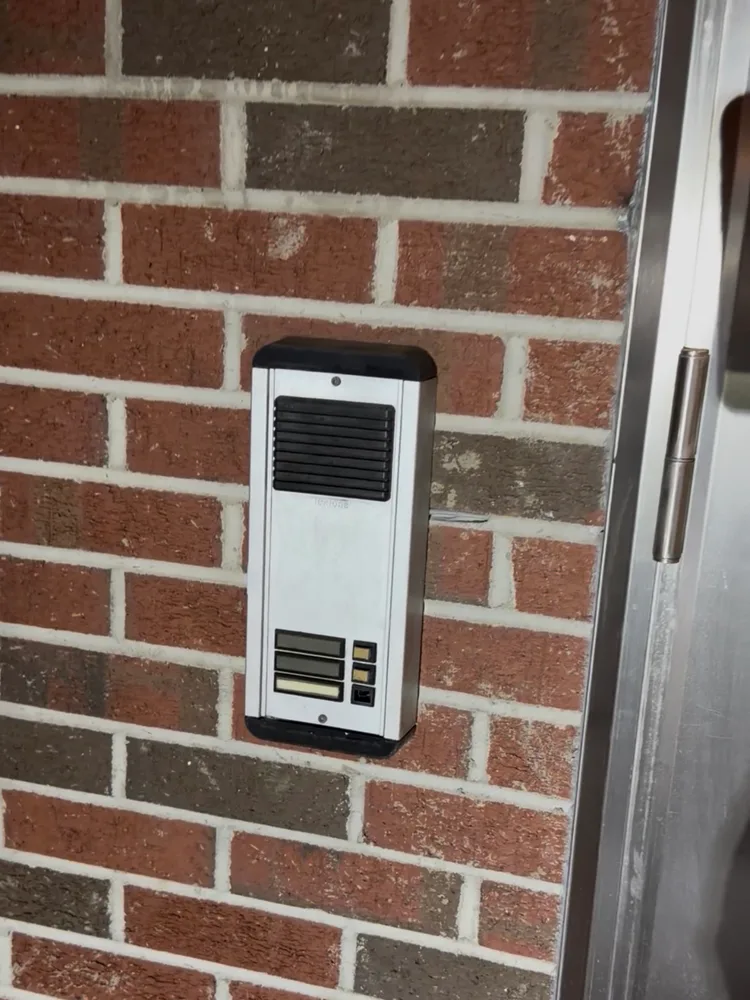 Original entrance intercom mounted on the home's brick wall before replacement